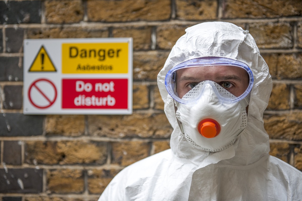 asbestos personal protective equipment covering hair and nose and mouth with warning danger sign in the background