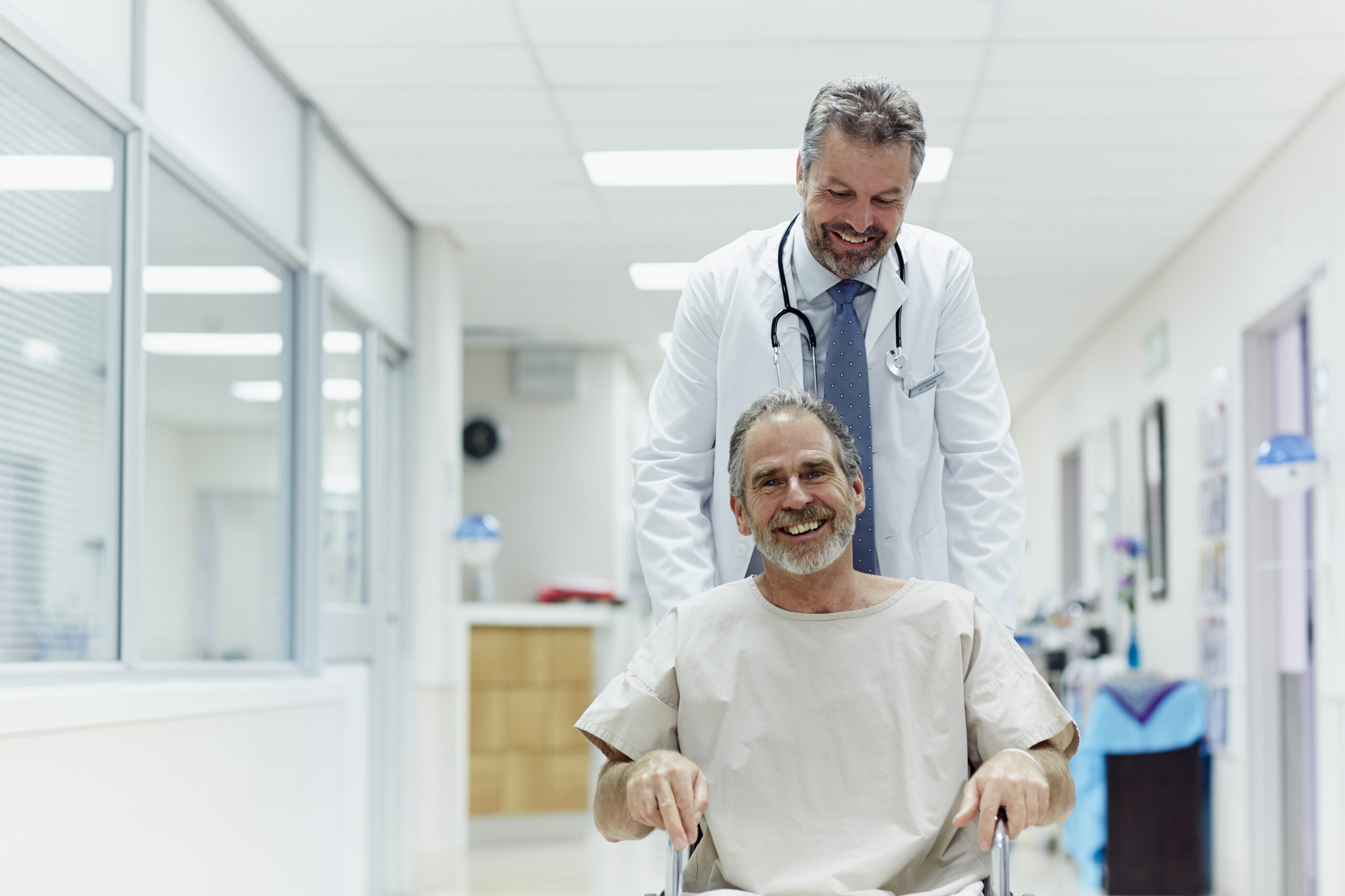 smiling patient being pushed in wheelchair by smiling doctor in a hospital