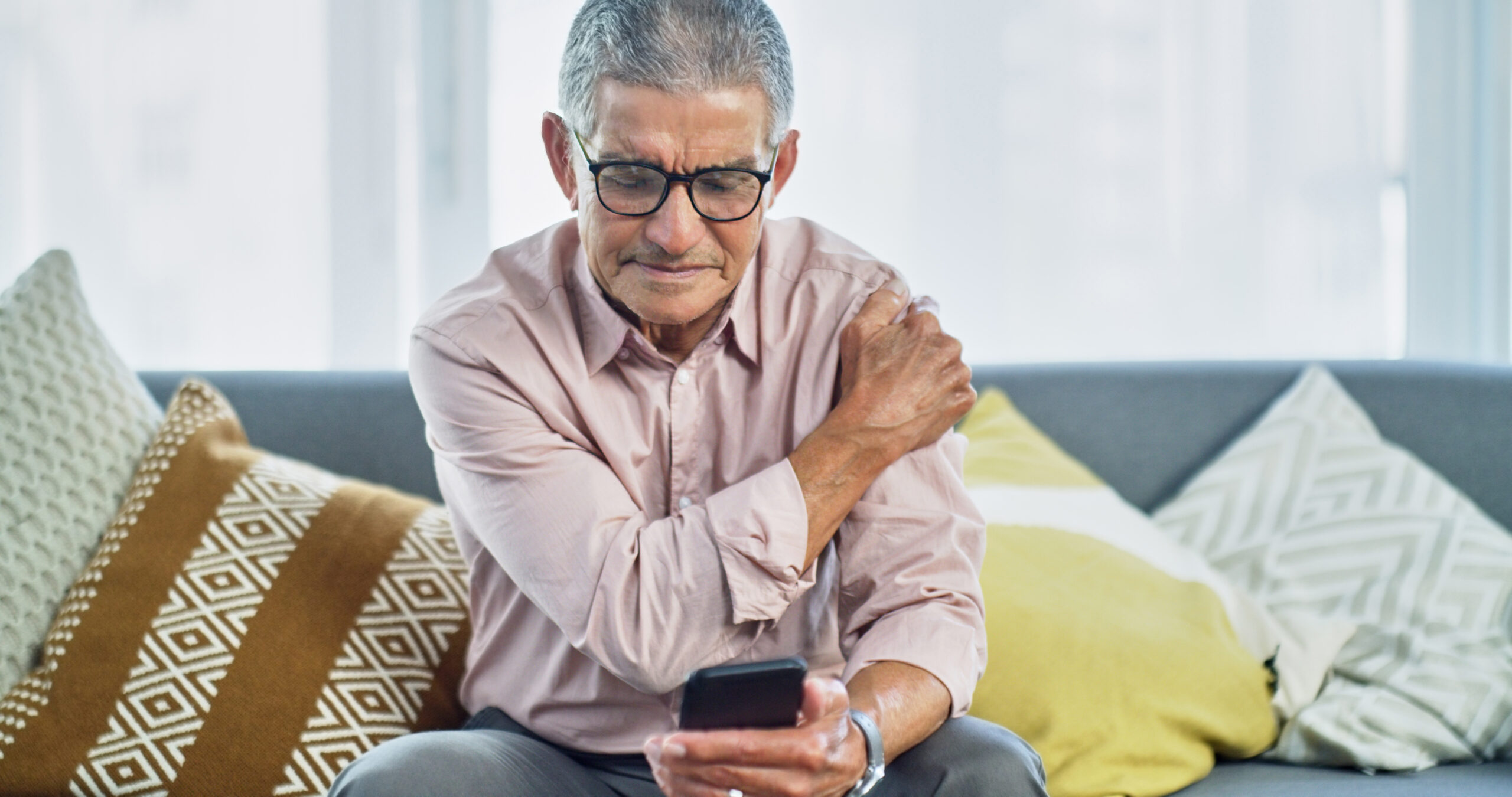 senior man experiencing shoulder pain while using a smartphone at home