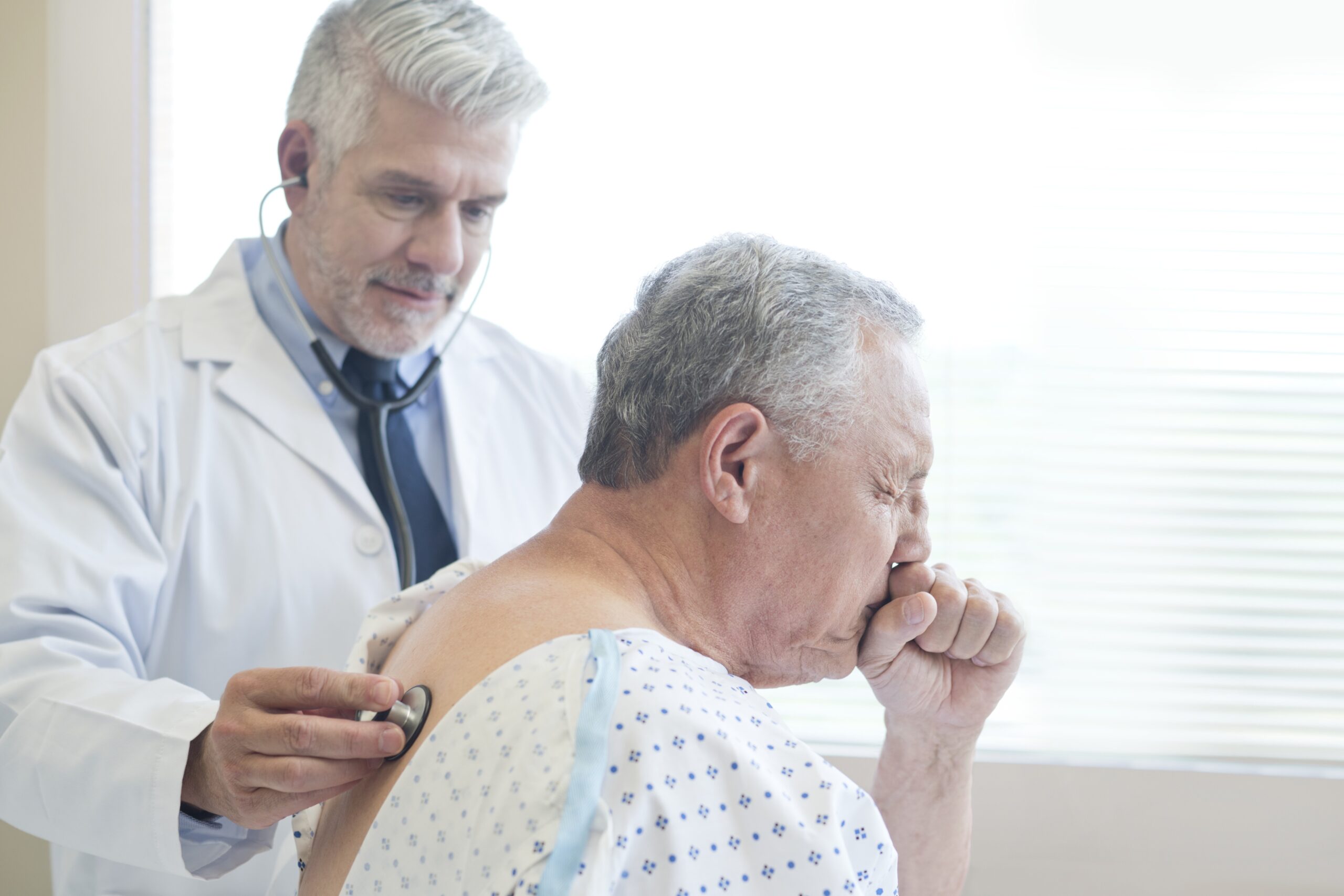 Male doctor examining mature man coughing