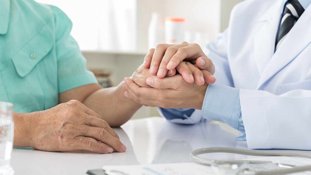 Doctor in white coat holding elderly patient's hand in an office