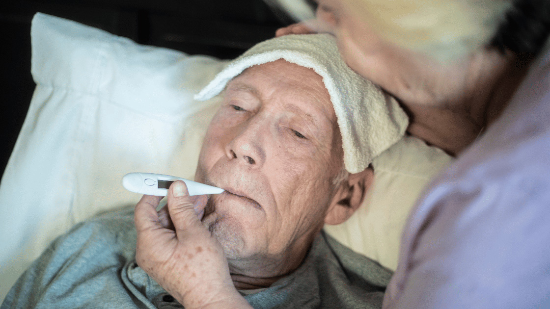 Elderly man with night sweats and fever cared by an older woman who is taking his temperature and putting a towel on his head