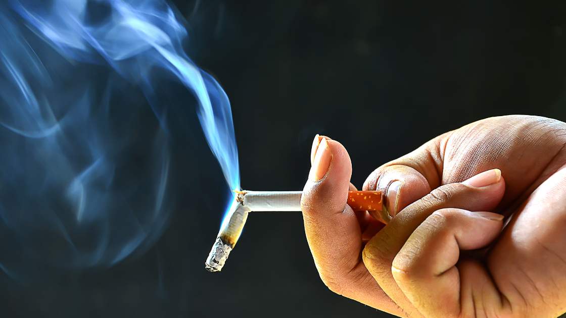 Person holding smoking asbestos filter cigarettes in front of dark background