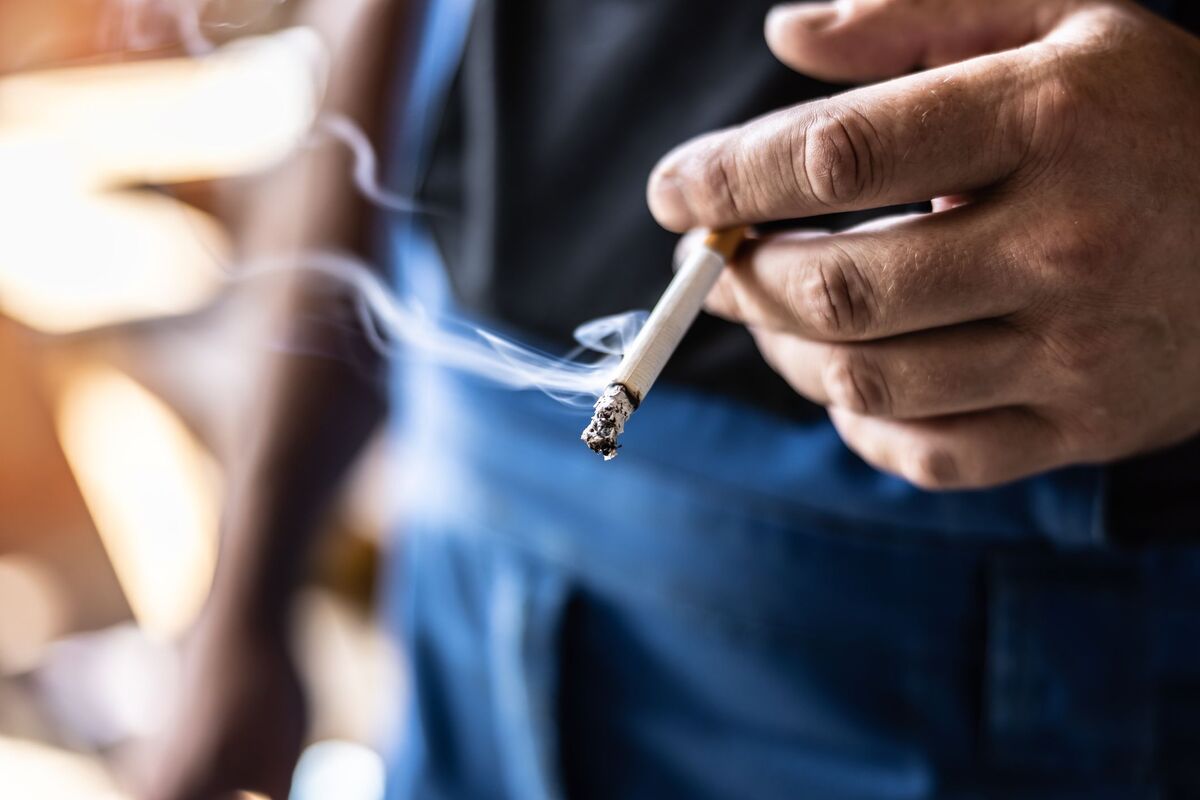 Man holding a burning cigarette in hand with blurred background